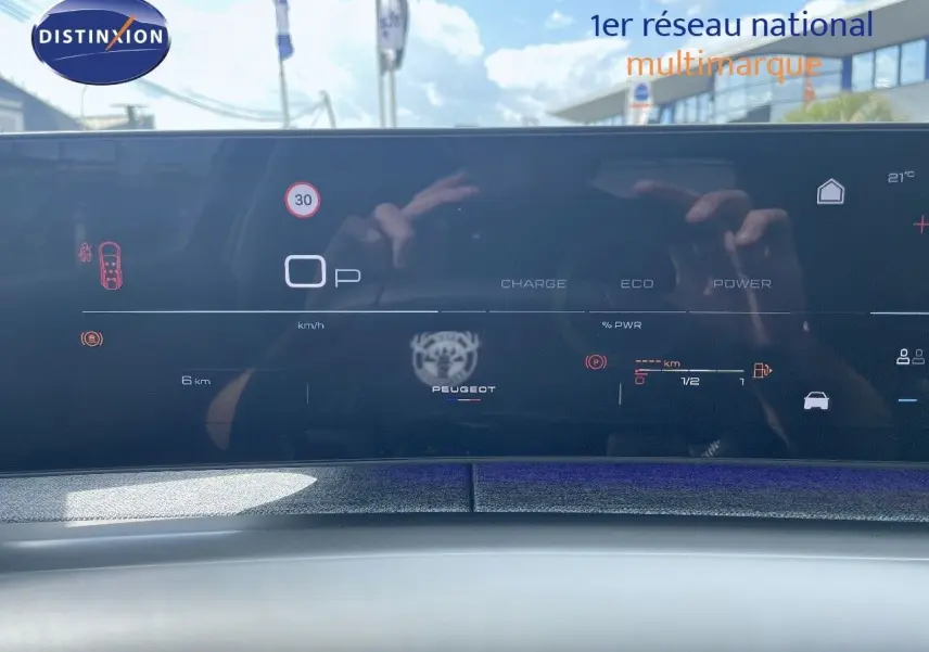 Tableau de bord numérique du Peugeot 5008 Hybrid 2025 affichant la vitesse et l'autonomie, avec reflet extérieur.
