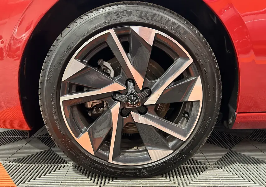 Gros plan sur la roue avant droite d’une Peugeot 308 rouge 2024 avec jante alliage bicolore et logo central Peugeot.