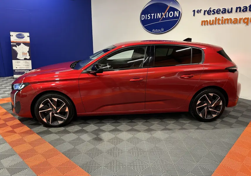 Profil latéral droit d'une Peugeot 308 rouge 2024, finition Allure avec jantes alliage et vitres teintées en intérieur showroom.