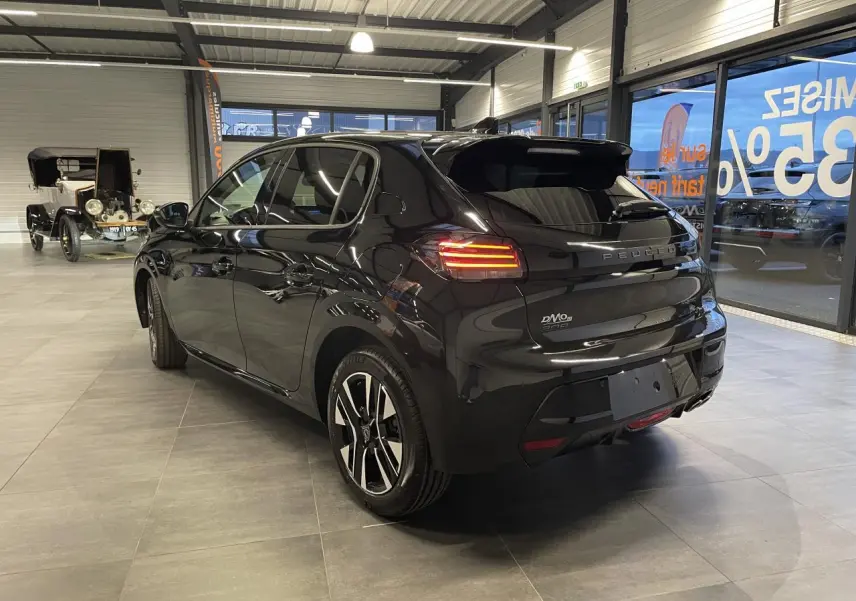 Vue 3/4 arrière droite d’une Peugeot 208 noire métallisée avec feux arrière allumés et jantes alliage bicolores en showroom.
