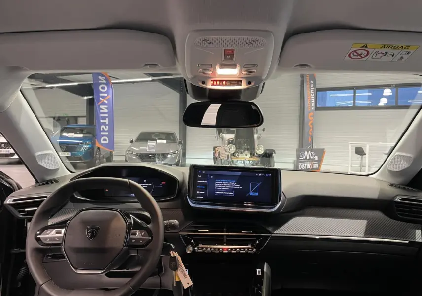Vue intérieure frontale du tableau de bord noir et gris clair de la Peugeot 208 1.2i Hybrid 2025 avec écran tactile central et volant compact cuir.