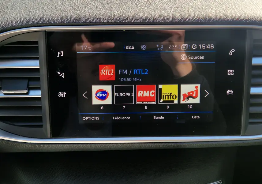 Écran tactile central du tableau de bord de la Peugeot 308 SW noire, affichant les stations radio FM avec interface moderne.