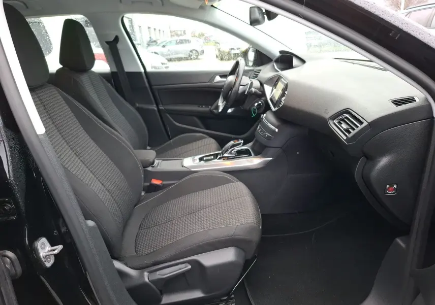 Vue intérieure côté gauche de la Peugeot 308 SW noire, montrant les sièges avant et le tableau de bord moderne.
