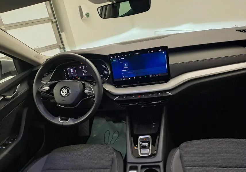 Vue intérieure avant de la Skoda Octavia Combi 2025, tableau de bord noir avec écran tactile central et volant multifonction.