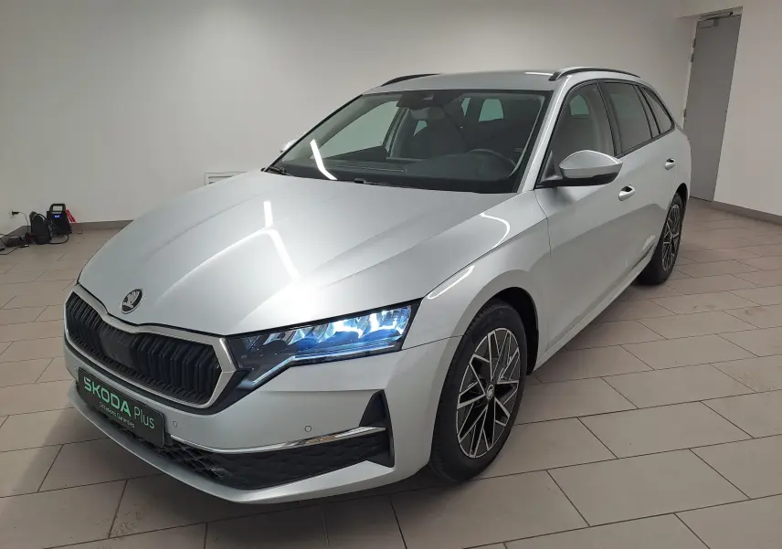 Vue 3/4 avant droite d'une Skoda Octavia Combi 2025 gris argent avec jantes alliage noires polies et phares LED allumés.