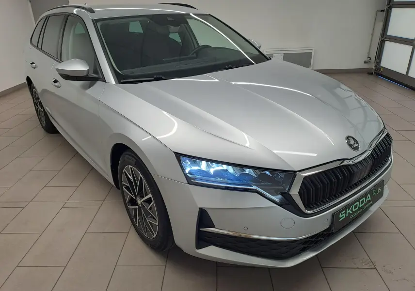 Vue 3/4 avant gauche d'une Skoda Octavia Combi gris argent avec phares allumés et jantes alliage noires polies.