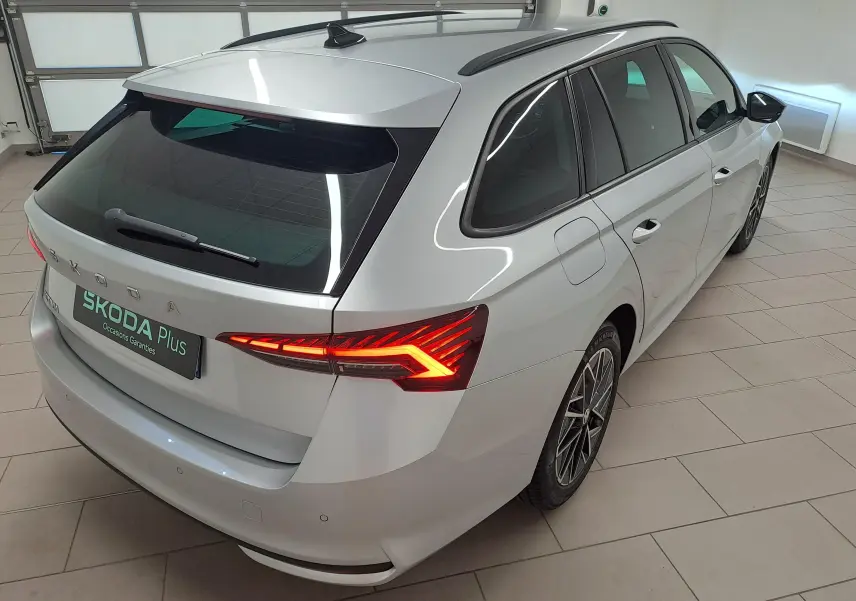 Vue 3/4 arrière droite d'une Skoda Octavia Combi gris argent avec feux arrière allumés et jantes alliage noires polies.