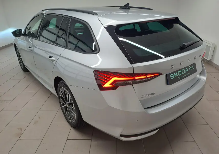 Vue 3/4 arrière droite d'une Skoda Octavia Combi gris argent avec feux arrière allumés et jantes alliage noires polies.