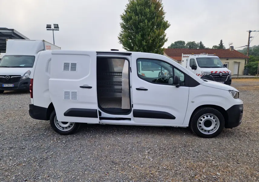 Vue de profil côté droit d’un Peugeot Partner blanc 2021 avec porte latérale coulissante ouverte montrant l’intérieur utilitaire.