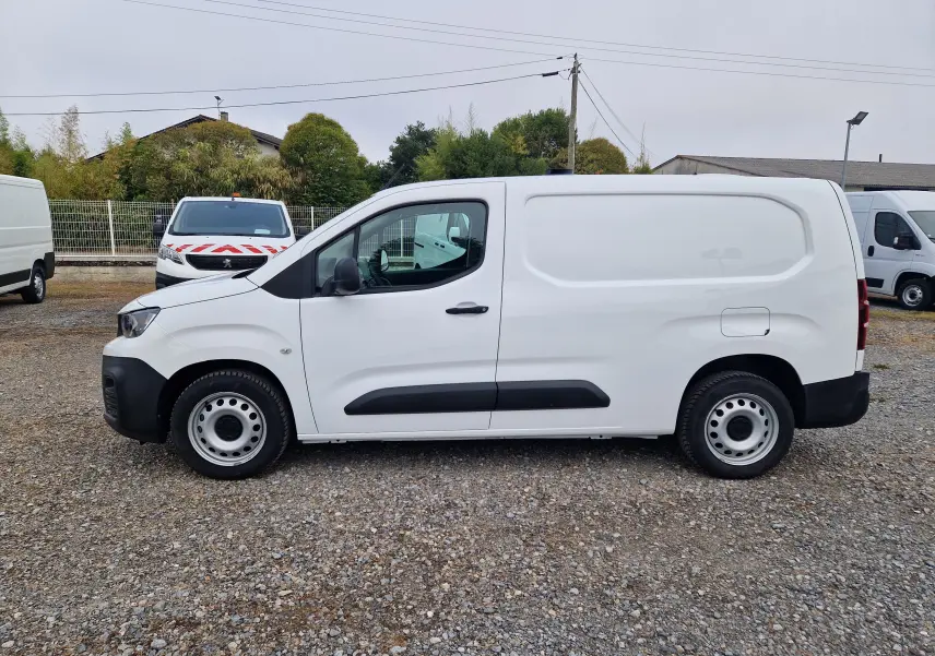 Vue de profil côté gauche d’un Peugeot Partner blanc 2021, version longue utilitaire avec protections noires sur les portières.