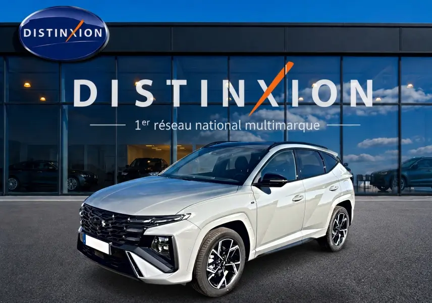 Vue 3/4 avant droite d'un Hyundai Tucson 2026 gris shadow avec jantes alu et calandre noire devant un showroom Distinxion.