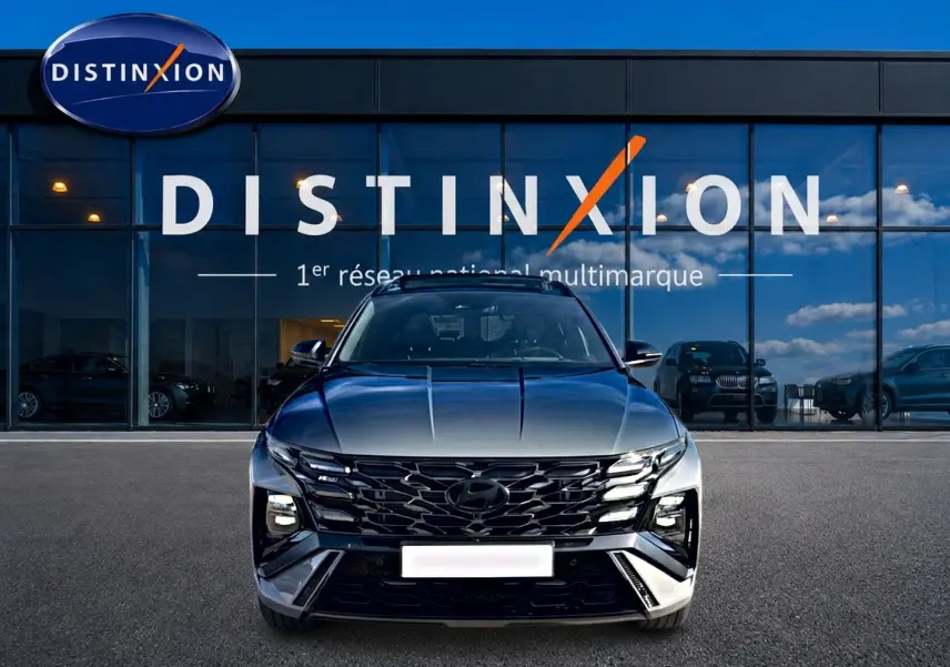 Vue avant d'un Hyundai Tucson 2026 gris shadow avec calandre noire et phares LED, devant une vitrine Distinxion.