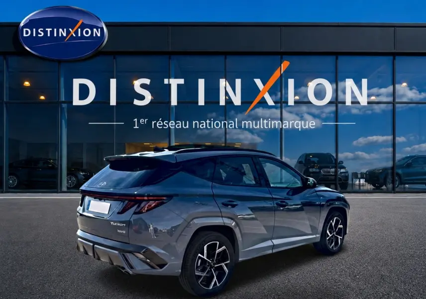 Vue 3/4 arrière droite d’un Hyundai Tucson gris shadow avec jantes alu et feux arrière LED, devant une vitrine Distinxion.
