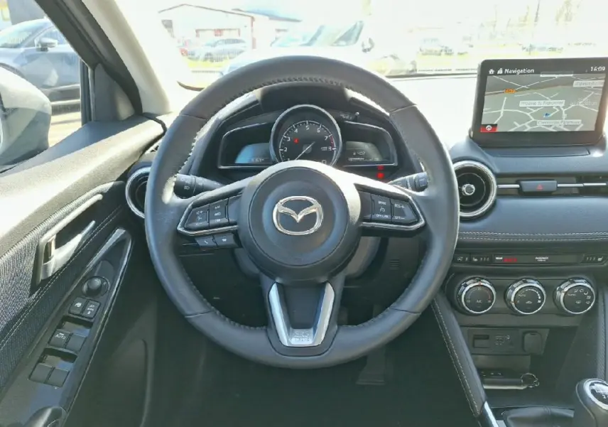 Vue intérieure centrée sur le volant cuir et tableau de bord avec écran tactile de la Mazda2 gris 2023.