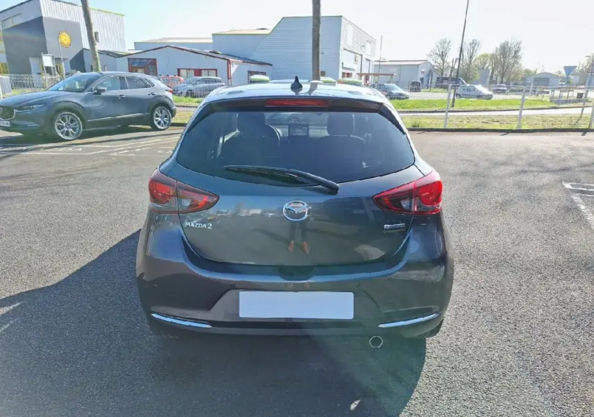 Vue arrière d'une Mazda2 gris métallisé 2023 avec feux rouges et lunette arrière teintée sur parking extérieur.