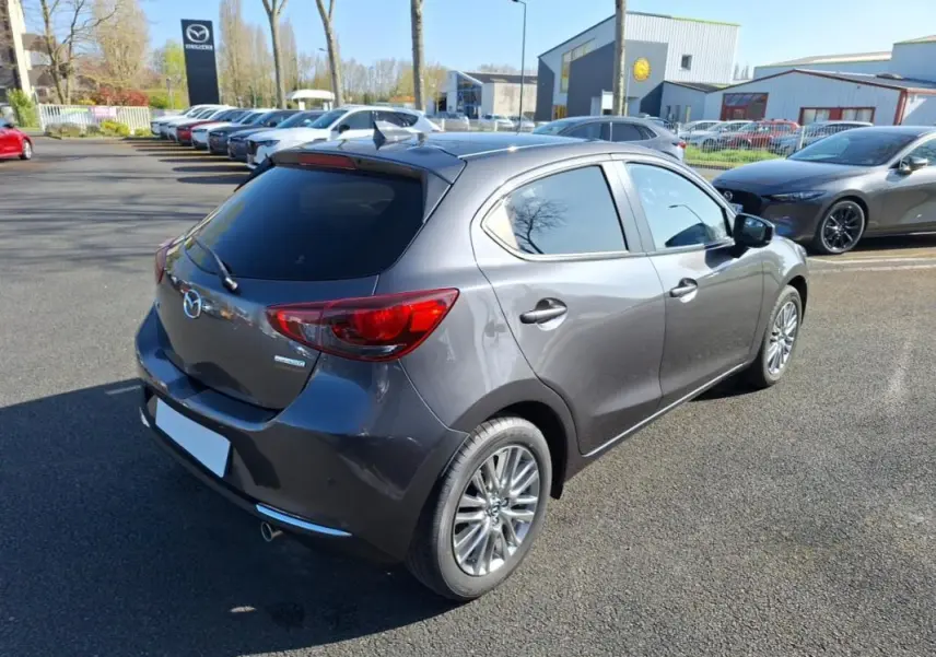 Vue 3/4 arrière droite d'une Mazda2 gris métallisé avec vitres surteintées et jantes aluminium sur parking.
