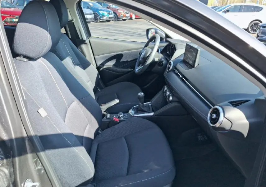 Intérieur avant de la Mazda2 2023, vue côté gauche, sièges noirs et tableau de bord avec écran tactile en relief.
