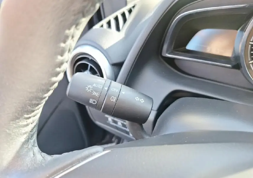 Gros plan sur le commodo des phares et clignotants à gauche du volant cuir dans l'habitacle gris de la Mazda2 2023.