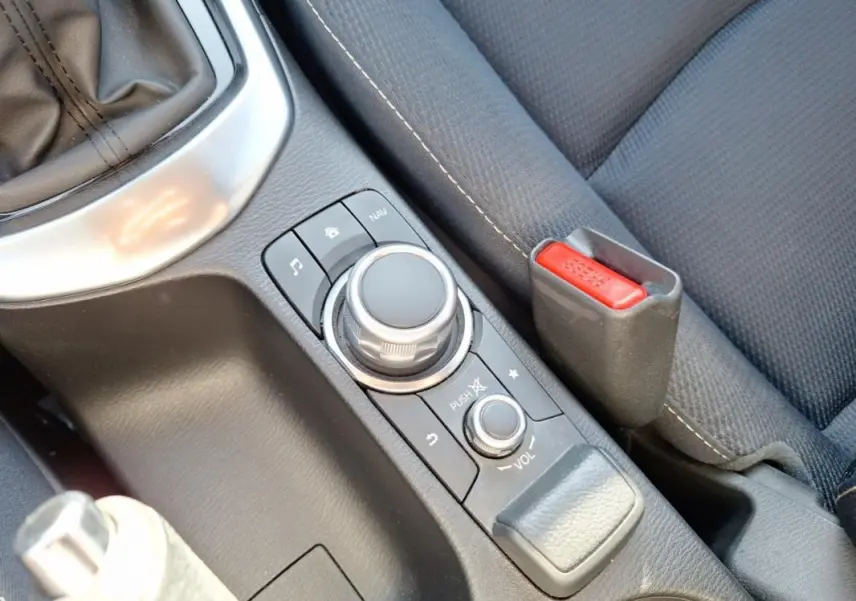 Gros plan sur la console centrale grise de la Mazda2 2023, avec molette de contrôle multimédia et frein à main.