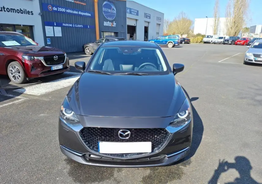 Vue frontale d'une Mazda2 gris métallisé 2023 avec calandre noire et phares LED circulaires visibles.
