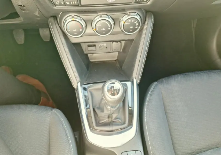 Vue plongeante sur la console centrale grise de la Mazda2 2023, avec levier de vitesse manuel et commandes de climatisation.