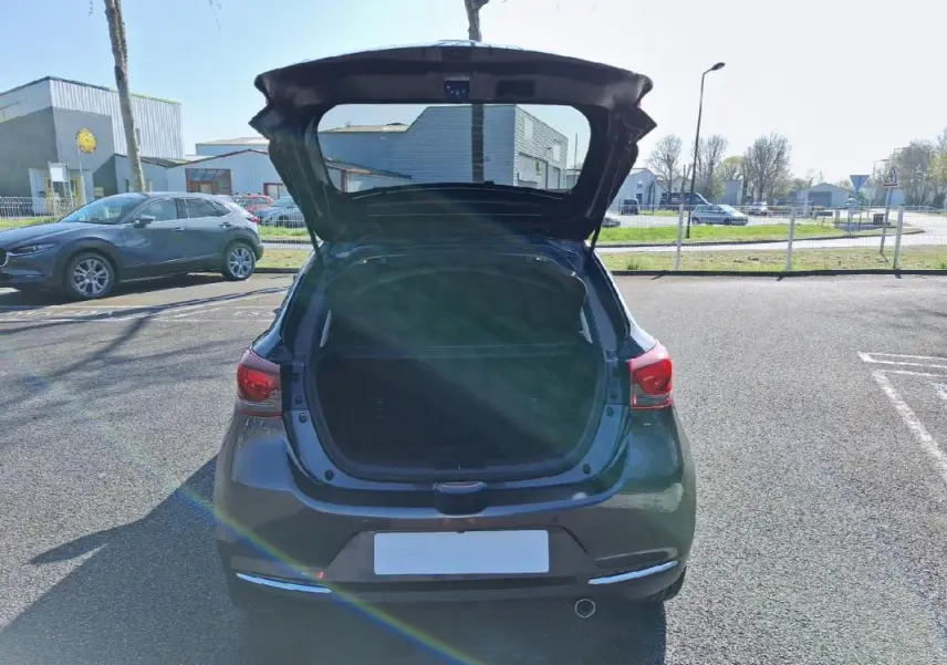 Vue arrière d'une Mazda2 gris avec coffre ouvert sur un parking ensoleillé.