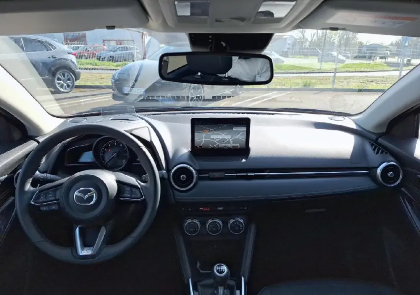 Vue intérieure avant du tableau de bord noir de la Mazda2 2023 avec écran tactile GPS et volant multifonctions cuir.