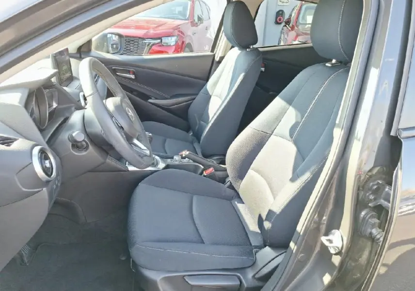 Intérieur avant de la Mazda2 gris 2023, vue côté conducteur montrant sièges tissu et tableau de bord moderne.