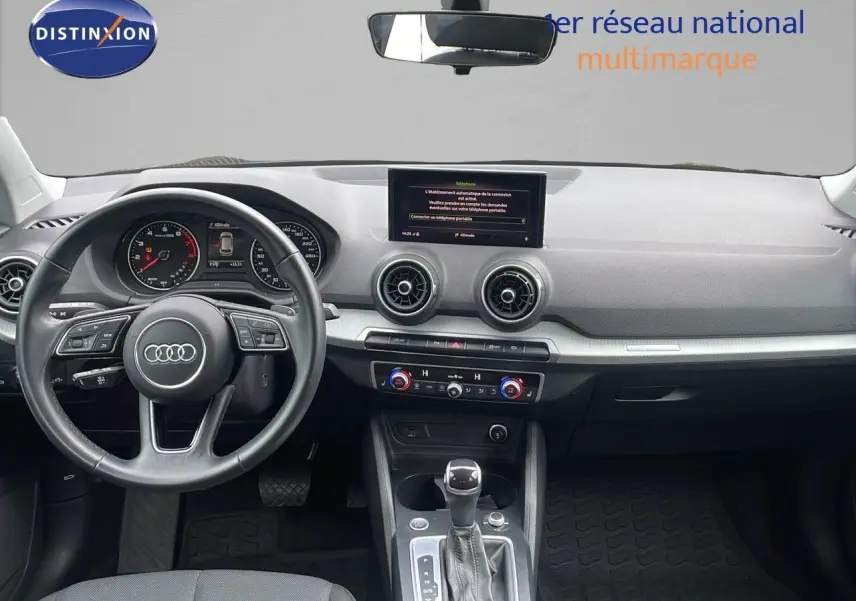 Vue intérieure de l'Audi Q2 35 TFSI S-Line 2023, tableau de bord et volant noir avec écran central et commandes climatisation.