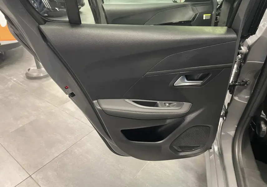 Vue intérieure de la porte arrière gauche gris selenium de la Peugeot 208 1.2i Hybrid Allure 2025 avec accoudoir et haut-parleur intégré.