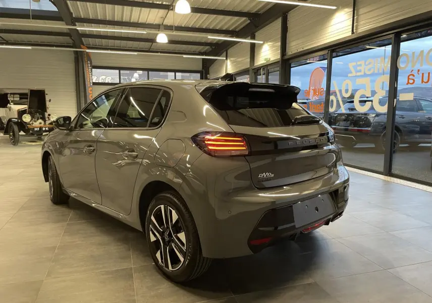 Vue 3/4 arrière droite d'une Peugeot 208 gris selenium avec feux arrière allumés en showroom.