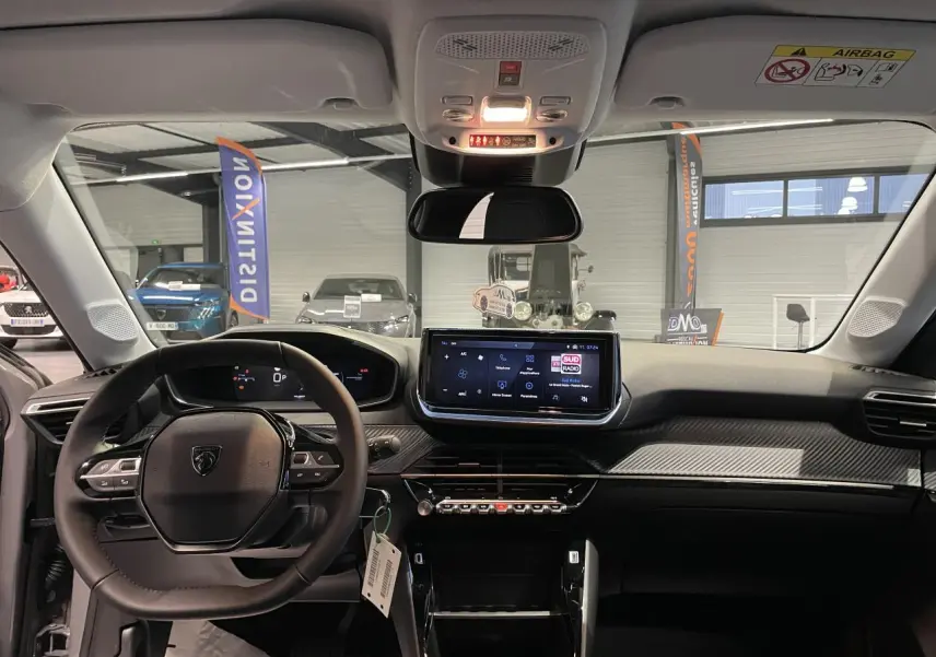 Vue intérieure avant du tableau de bord et volant noir de la Peugeot 208 1.2i Hybrid 2025 avec écran tactile central.