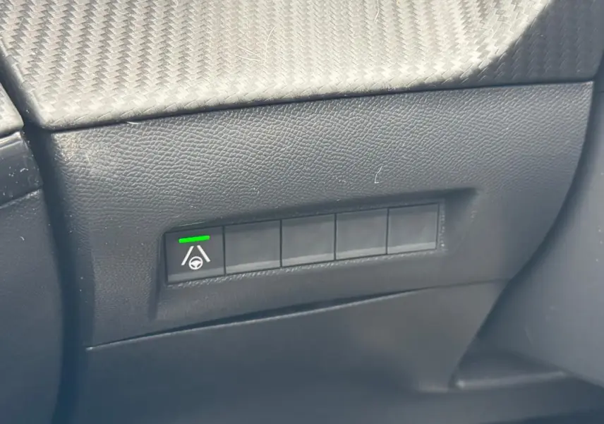Gros plan sur le bouton d’aide au maintien de voie avec témoin vert dans l’habitacle noir d’une Peugeot 208 Hybrid 110 e-DCS6 GT.