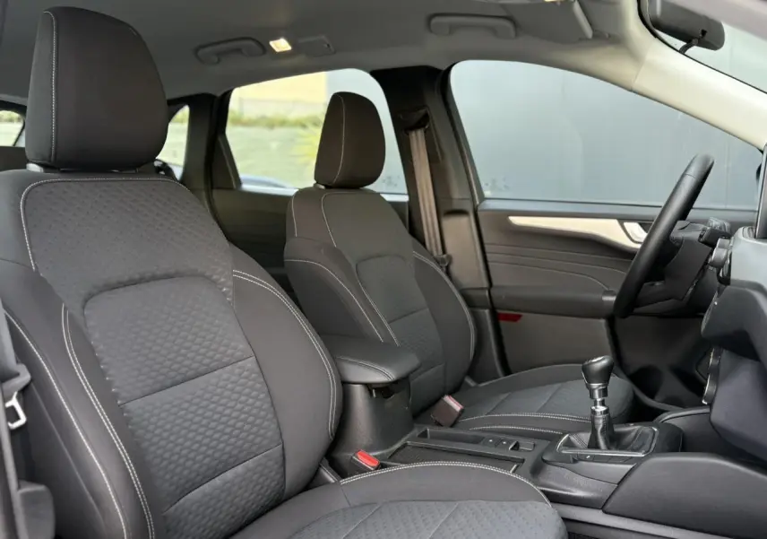 Vue intérieure côté droit du Ford Kuga 2024 noir Obsidien, montrant les sièges avant en tissu avec surpiqûres blanches et levier de vitesses manuel.