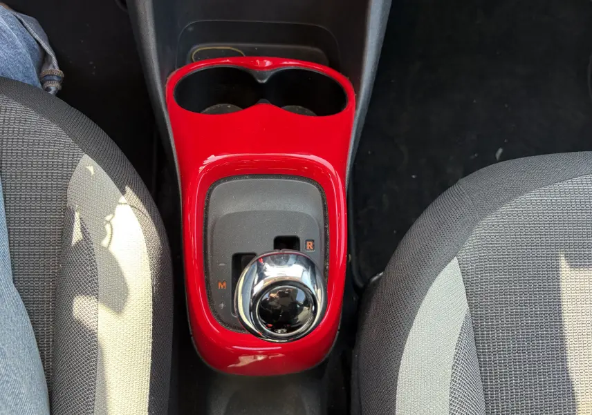 Vue plongeante sur la console centrale rouge et le levier de vitesse chromé entre les sièges avant gris de la Toyota Aygo MC blanche.