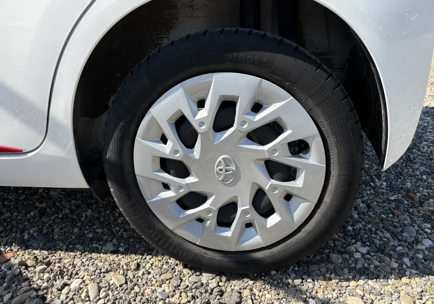 Gros plan sur la roue avant droite d'une Toyota Aygo MC blanche, avec enjoliveur argenté au design géométrique.