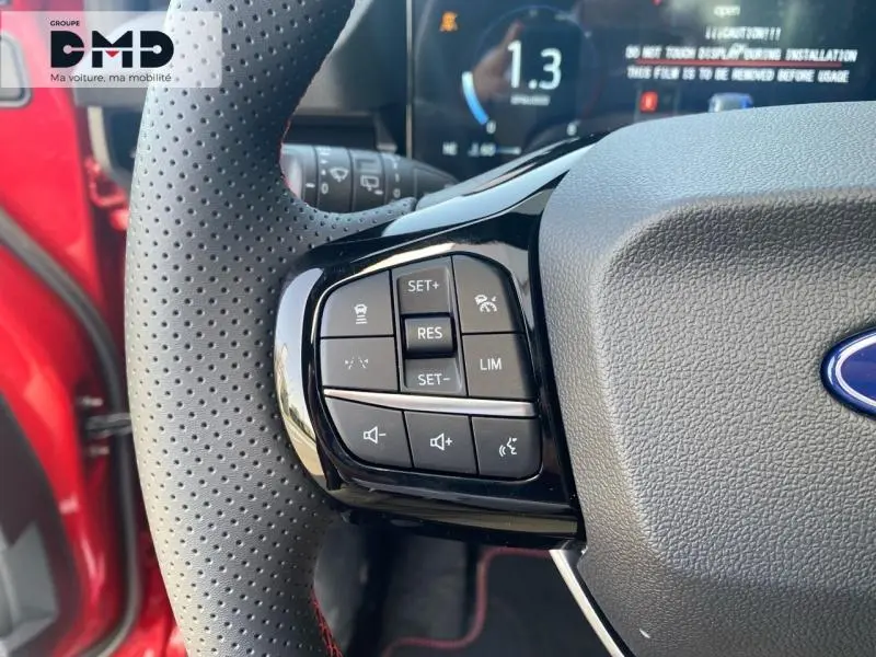 Gros plan sur les commandes au volant côté gauche d'un Ford Puma rouge, avec affichage numérique en arrière-plan.