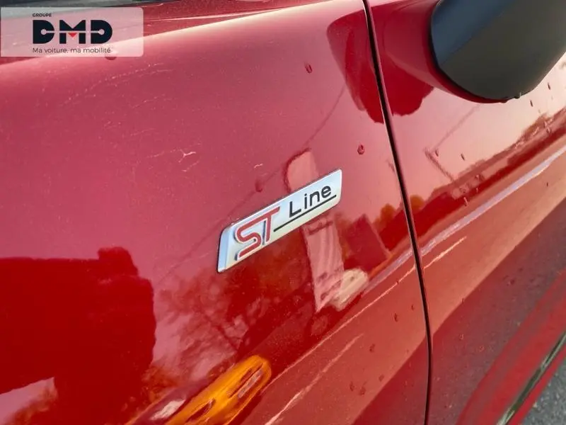 Gros plan sur l'écusson ST-Line côté gauche d'une Ford Puma rouge métallisée avec gouttes d'eau visibles.