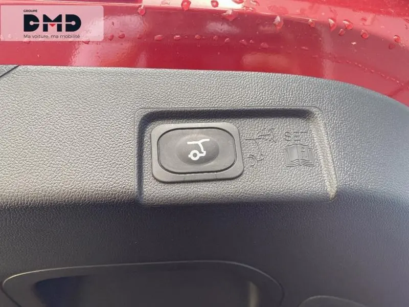 Gros plan sur le bouton d'ouverture électrique du coffre, sur la partie intérieure rouge métallisée du Ford Puma.