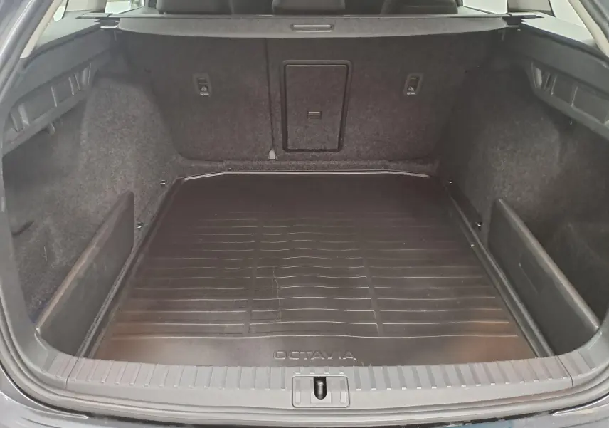 Coffre ouvert vu de l'arrière d'une Skoda Octavia Combi 2024 gris graphite, avec tapis de coffre noir marqué Octavia.