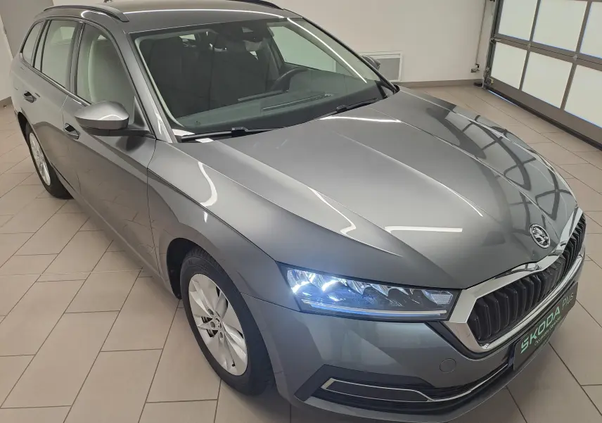 Vue 3/4 avant droit d'une Skoda Octavia Combi 2024 gris graphite avec phares allumés dans un garage.