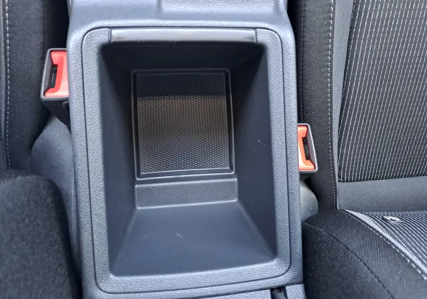 Gros plan sur le rangement central entre les sièges avant d'une Skoda Octavia Combi 2024 gris graphite, avec ceintures rouges visibles.