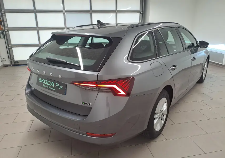 Vue 3/4 arrière droite d'une Skoda Octavia Combi 2024 gris graphite avec feux arrière LED allumés en intérieur showroom.