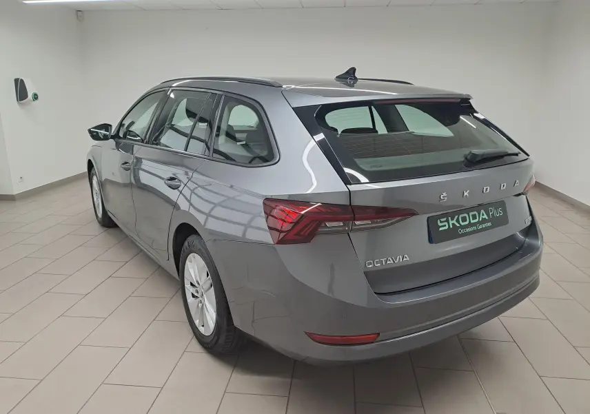 Vue 3/4 arrière droite d'une Skoda Octavia Combi 2024 gris graphite métallisé dans un showroom lumineux.