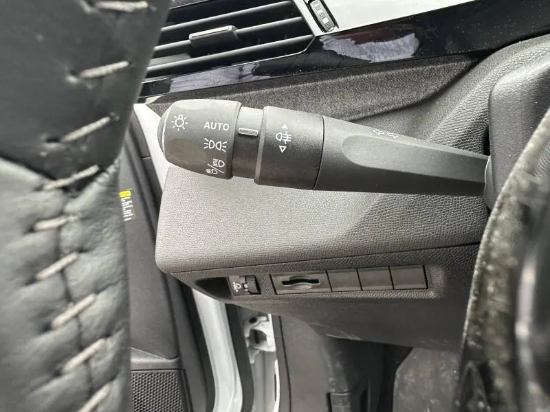 Gros plan sur la commande des phares et clignotants côté gauche du tableau de bord noir d'une Peugeot 308 blanche.