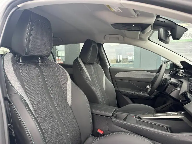Vue intérieure côté conducteur de la Peugeot 308 1.2 Hybrid 145ch Allure en tissu gris avec accoudoir central et volant multifonction.
