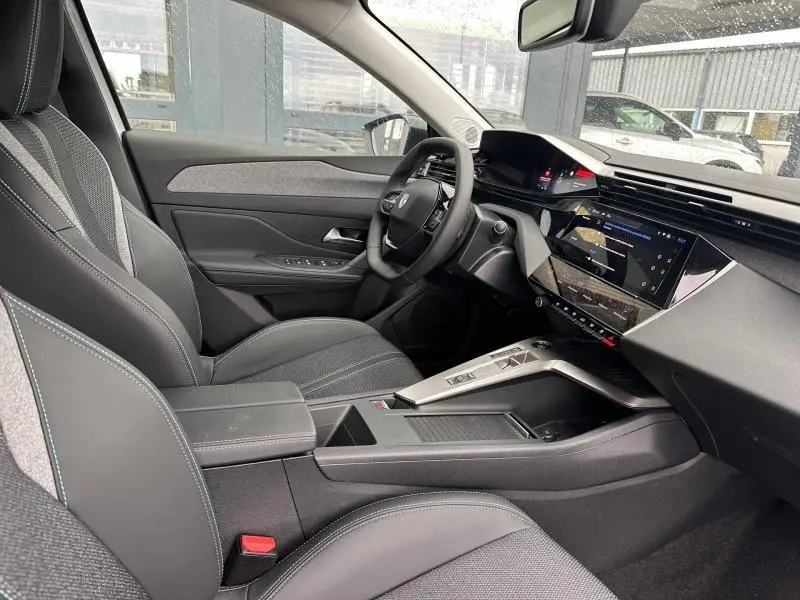 Intérieur avant droit de la Peugeot 308 Hybrid 2025, sièges en tissu et cuir noir avec tableau de bord moderne et écran tactile.