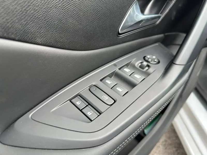 Gros plan sur la commande des vitres et rétroviseurs côté conducteur de la Peugeot 308 blanche, avec surpiqûres blanches.