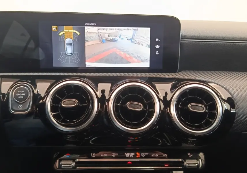 Vue intérieure du tableau de bord noir brillant de la Mercedes Classe A 180 d avec écran tactile et aérateurs ronds chromés.