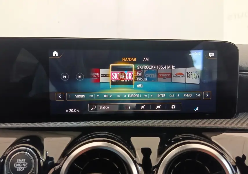 Écran tactile central allumé sur radio FM dans l’habitacle d’une Mercedes Classe A gris clair, vue de face rapprochée.